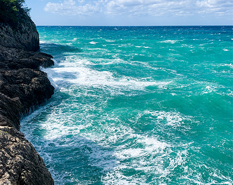Turquoise blue waters with white wave caps crashing against a rock cliff